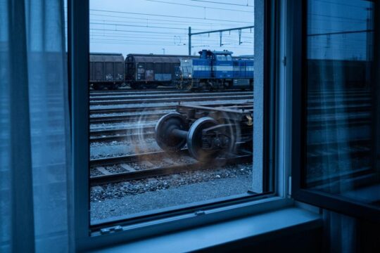 Blick aus einem Fenster auf den Lärm Rangierbahnhof Muttenz bei Dämmerung. Quietschende Stahlräder von Güterwagen visualisieren die Störung der Nachtruhe.