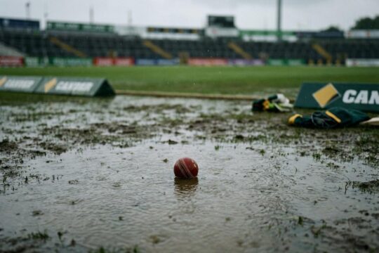 Regen durchnässt einen Cricketplatz mit Pfützen und verlassenem Ball, was das abrupte T20 WM Aus für Irland und Australien durch Wetterchaos symbolisiert.