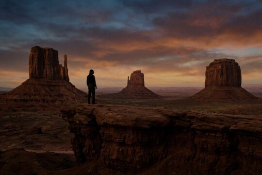 Lieutenant Joe Leaphorn blickt in der Dämmerung nachdenklich über das Monument Valley, das die unheilvolle Atmosphäre von Dark Winds Staffel 4 symbolisiert.