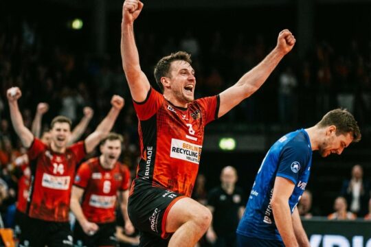 BR Volleys Spieler jubelt mit erhobenen Armen triumphierend nach dem BR Volleys Sieg Friedrichshafen. Ein Gegner senkt enttäuscht den Kopf.