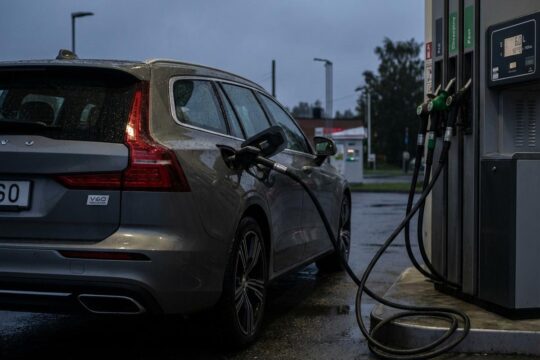 Moderner Plug-in-Hybrid an der Tankstelle. Benzinschlauch steckt; Anzeige 6.0 L/100km. Ungenutztes Ladekabel zeigt hohen Plug-in-Hybrid Verbrauch.