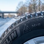 Nahaufnahme eines modernen Winterreifens mit Alpine-Symbol auf leicht verschneiter deutscher Fahrbahn. Das Bild verdeutlicht die Winterreifenpflicht Deutschland.