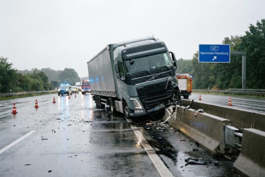 Massiv beschädigter Lkw lehnt nach Lkw-Unfall A7 Seesen an zersplitterter Betonschutzwand. Regennasse Fahrbahn, leichte Verschmutzung, Blaulichter der Einsatzkräfte im Hintergrund.