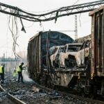 Folgen des Güterzug Brand Magdeburg: Verkohlter Güterwaggon mit Autoresten, zerstörte Oberleitung und Trümmer. Arbeiter beginnen mit der Inspektion.