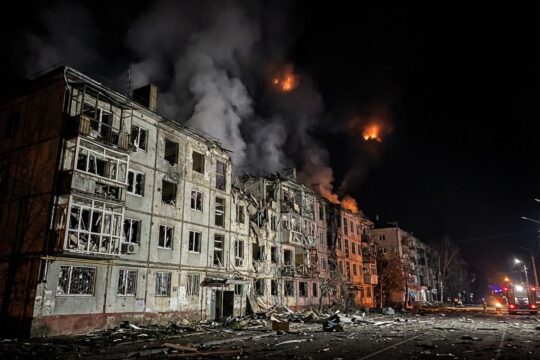 Ein stark beschädigtes Wohnhaus bei Nacht in einer ukrainischen Großstadt. Rauch und Trümmer zeugen von den russischen Raketenangriffen auf die Ukraine.