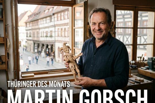 Thüringer des Monats Martin Gobsch, der Puppenschnitzer, präsentiert in seiner Werkstatt eine filigrane Holzpuppe. Im Hintergrund die historische Krämerbrücke.